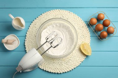 Açık mavi ahşap masa üzerinde çırpılmış krema, yumurta ve diğer ürünlerle el çırpıcı düz yatıyordu.