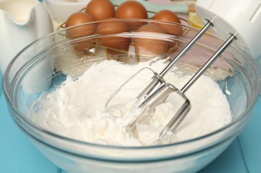 Çırpılmış çırpılmış çırpılmış krema, açık mavi masada yumurta ve süt, yakın plan.