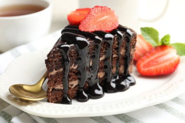 Çilek, kaşık ve çay ile servis edilen bir parça çikolatalı kek.