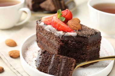 Çilekli, bademli ve masada çay bulunan bir dilim lezzetli çikolatalı pasta.