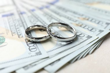 İki gümüş alyans ve bir dolarlık banknotlar beyaz masada, yakın plan.