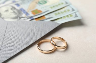 İki altın alyans, bir dolarlık banknotlar ve beyaz masanın üzerindeki zarf, yakın plan.