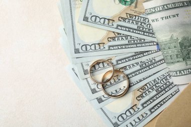 İki altın alyans, bir dolarlık banknotlar ve beyaz masadaki zarf, üst manzara. Metin için boşluk
