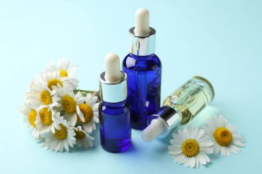 Açık mavi arka planda gerekli yağ ve papatya çiçekleri, yakın plan.