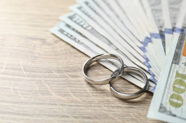 Gümüş alyanslar ve dolar banknotları ahşap masada, yakın plan. Metin için boşluk