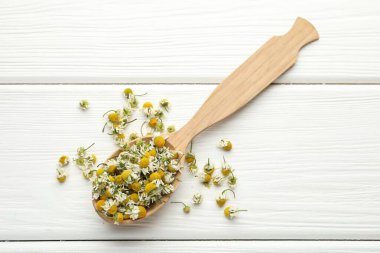 Beyaz ahşap masada kaşıkta papatya çiçekleri, üst manzara.
