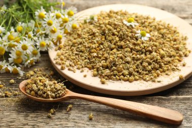 Kuru, taze papatya çiçekleri ve tahta masada kaşık, yakın plan.