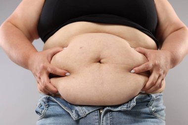 Gri arka planda aşırı göbek yağlı kadın, yakın plan. Aşırı kilolu