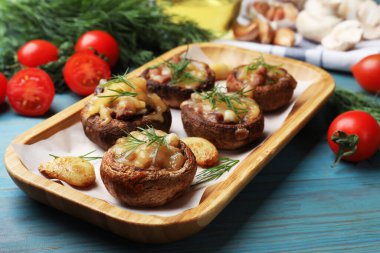 Eritilmiş peynirli, sarımsaklı ve dereotlu leziz mantarlar açık mavi ahşap masada, yakın plan.