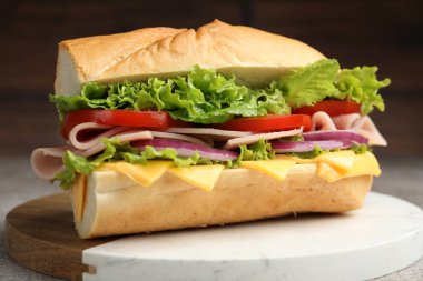 Gri desenli masada jambonlu, peynirli ve sebzeli baget sandviç, bulanık kahverengi arka plan, yakın plan.