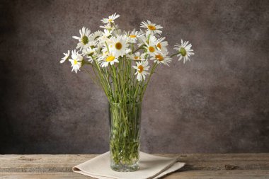 Tahta masadaki vazoda, kahverengi desenli arka planda birçok güzel papatya çiçeği, yakın plan.