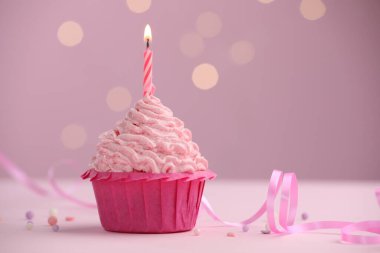 Masanın üzerinde, pembe arka planda, bulanık ışıklarla yanan mum. Metin için boşluk