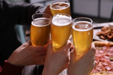 Arkadaşlar masada bira bardaklarını tokuşturur, yakın plan