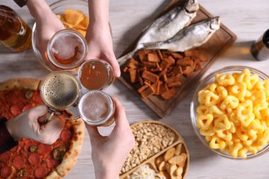 Arkadaşlar beyaz ahşap masada bira bardaklarını tokuşturuyor.