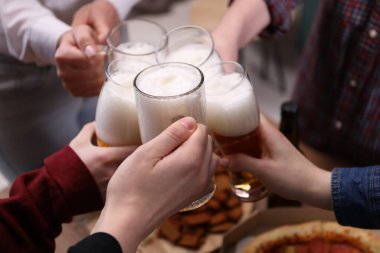 Arkadaşlar masada bira bardaklarını tokuşturur, yakın plan