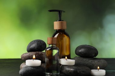 Islak taşlı spa kompozisyonu, kozmetik ürünleri ve koyu yeşil arka planda yanan mumlar, yakın plan