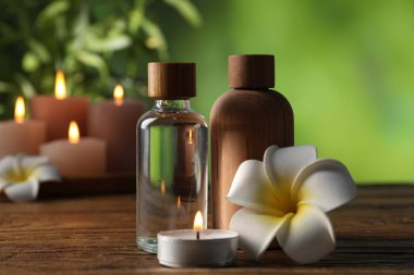 Kozmetik ürünleri, çiçekler ve ahşap masada yanan mumlarla kaplıca bileşimi bulanık yeşil arka plan, yakın plan