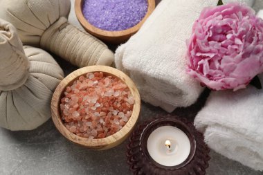 Gri desenli masa üzerinde bitki torbaları, deniz tuzu ve havlular içeren spa kompozisyonu.