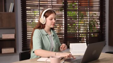 Kulaklık takan genç bir öğrenci içeride çalışırken dizüstü bilgisayar kullanıyor.