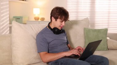 Ergen öğrenci evdeki kanepede çalışırken dizüstü bilgisayar kullanıyor.