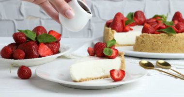 Beyaz ahşap masadaki leziz peynirli kekin üzerine sos döken kadın.