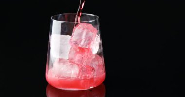 Lezzetli vişneli gazozu buzlu bardağa dolduran ve masada siyah arka planda böğürtlen ekleyen kadın.