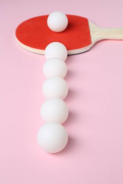 Pembe arka planda pinpon raketi ve toplar, yakın plan.