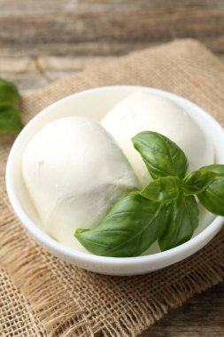 Ahşap masada lezzetli mozzarella peyniri ve fesleğen, yakın plan.