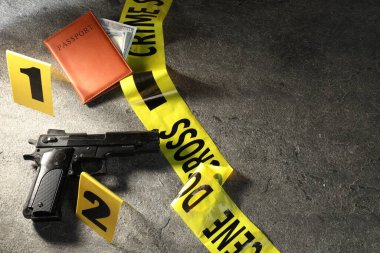 Adli tıp uzmanı. Sarı olay yeri bandı, silah, pasaport ve para gri masada, düz yerde. Metin için boşluk