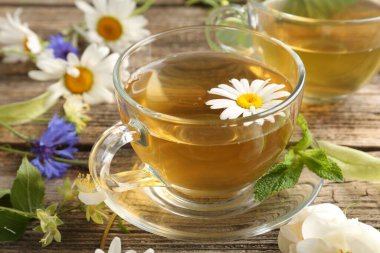 Cam bardaklarda aromatik bitki çayı, ahşap masada nane ve çiçekler, yakın plan.