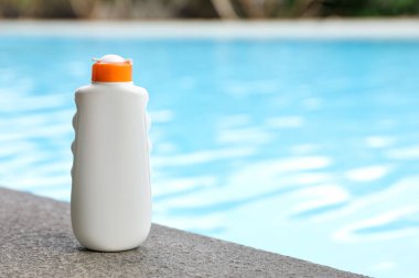 Yüzme havuzunun yakınındaki taş yüzeyde bir şişe güneş koruması ürünü, metin için yer
