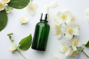 Temel yağ, yasemin çiçekleri ve beyaz arka planda yeşil yapraklar.