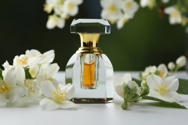 Beyaz masadaki bir şişe parfüm ve yasemin çiçekleri bulanık arka planda, yakın plan