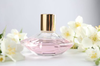 Beyaz masada bir şişe parfüm ve yasemin çiçeği, yakın plan.