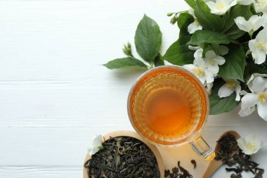 Cam bardakta Aromatik yasemin çayı, beyaz ahşap masada çiçekler ve yapraklar, düz yatış. Metin için boşluk