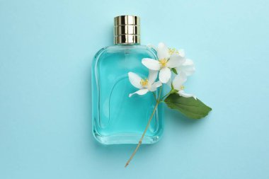 Bir şişe parfüm, güzel yasemin çiçekleri ve açık mavi arka planda yeşil yaprak.