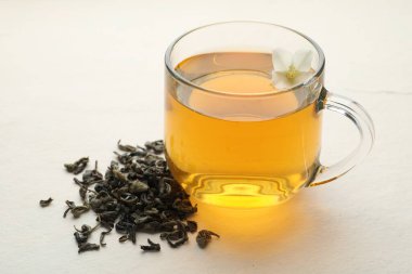 Aromatik yasemin çayı cam bardakta, çiçek ve kuru yapraklar beyaz masada, yakın plan.