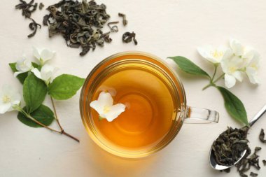 Cam bardakta Aromatik yasemin çayı, beyaz masada çiçekler ve yapraklar, düz uzanmış