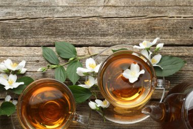 Cam fincanlarda, çaydanlıkta, çiçeklerde ve yeşil yapraklarda ahşap masada yassı yasemin çayı.