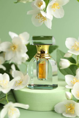 Yeşil arka planda bir şişe parfüm ve yasemin çiçeği, yakın plan.