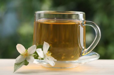 Lezzetli yasemin çayı fincanda ve çiçekler beyaz ahşap masada, yakın plan.