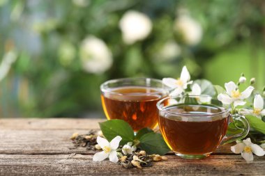 Lezzetli yasemin çayı fincanlarda, kuru yapraklar ve ahşap masada çiçekler, yakın plan. Metin için boşluk
