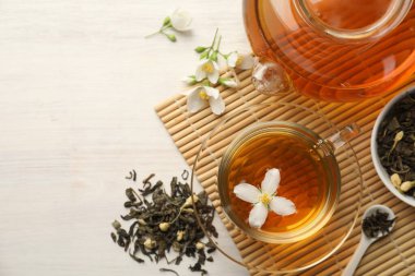 Lezzetli yasemin çayı fincanda, çaydanlıkta, kuru yapraklarda ve beyaz ahşap masada, düz yerde. Metin için boşluk