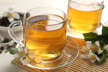 Lezzetli yasemin çayı, kuru yapraklar ve beyaz ahşap masa üzerinde çiçekler, yakın plan.