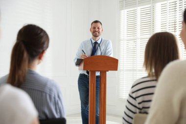Oturma odasında seyirci önünde konuşma yapan bir adam.