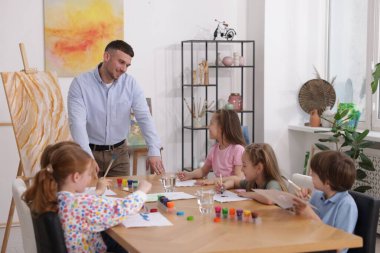 Çocuklara resim dersinde resim yapmayı öğreten bir adam.