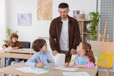 Çocuklara resim dersinde resim yapmayı öğreten bir adam.