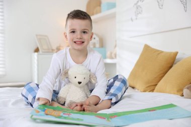 Yatma vakti. Oyuncak koyunlarıyla yatakta kitap okuyan sevimli bir çocuk.