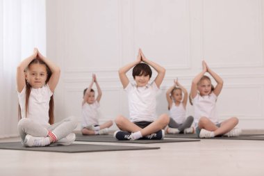Sınıftaki minderler üzerinde yoga yapan bir grup çocuk.