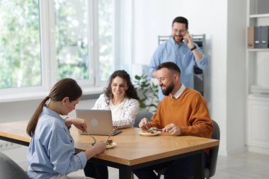 İş arkadaşları ofiste yemek yiyor ve sohbet ediyorlar.